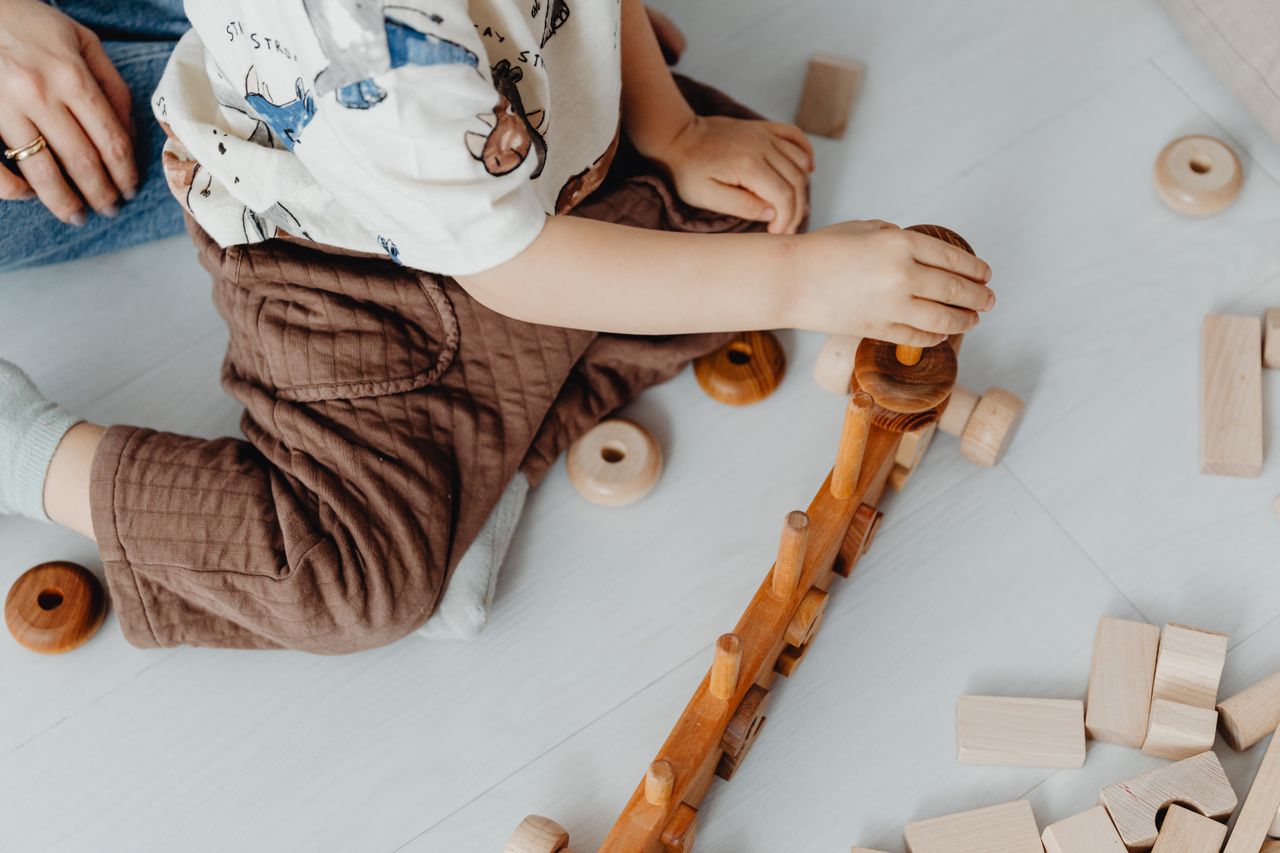 A child playing with wooden blocks and toys on the floor, engaging in creative play.